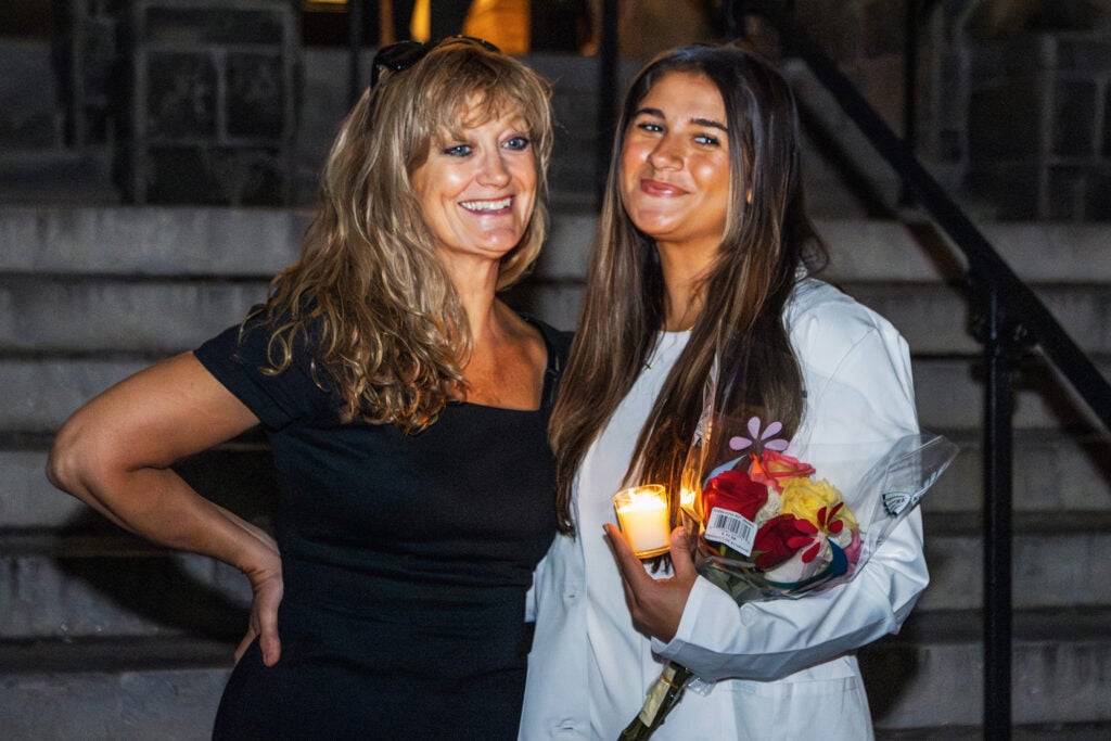 A nursing student in her white coat stands on the steps of Healy Hall with her mother who is an alum