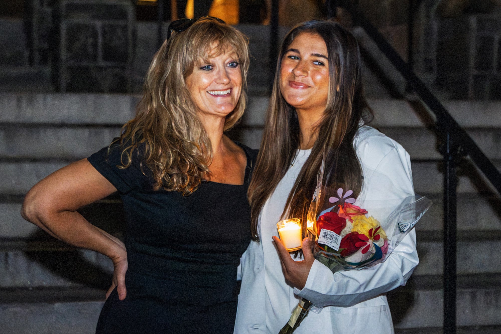 A nursing student in her white coat stands on the steps of Healy Hall with her mother who is an alum