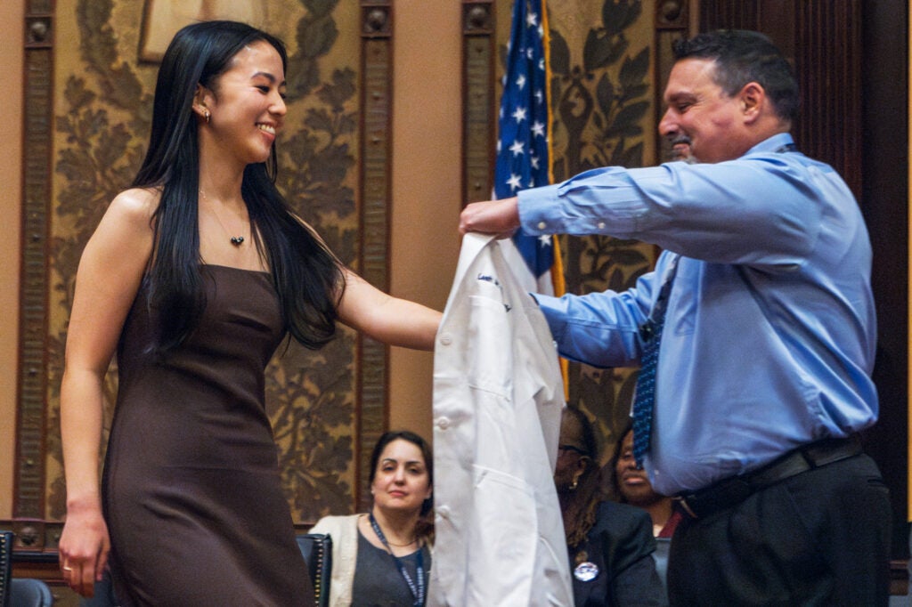 A faculty member helps a nursing student put on her white coat