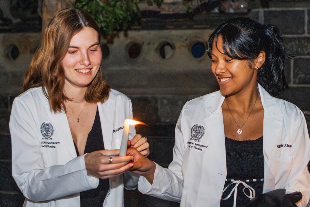 A nursing student in white coat passes a lit candle to another nursing student in white coat