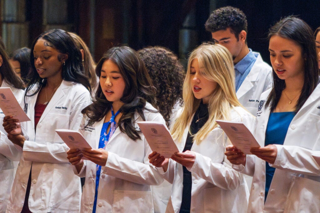 Nursing students stand together and recite an oath from a program that each of them is holding