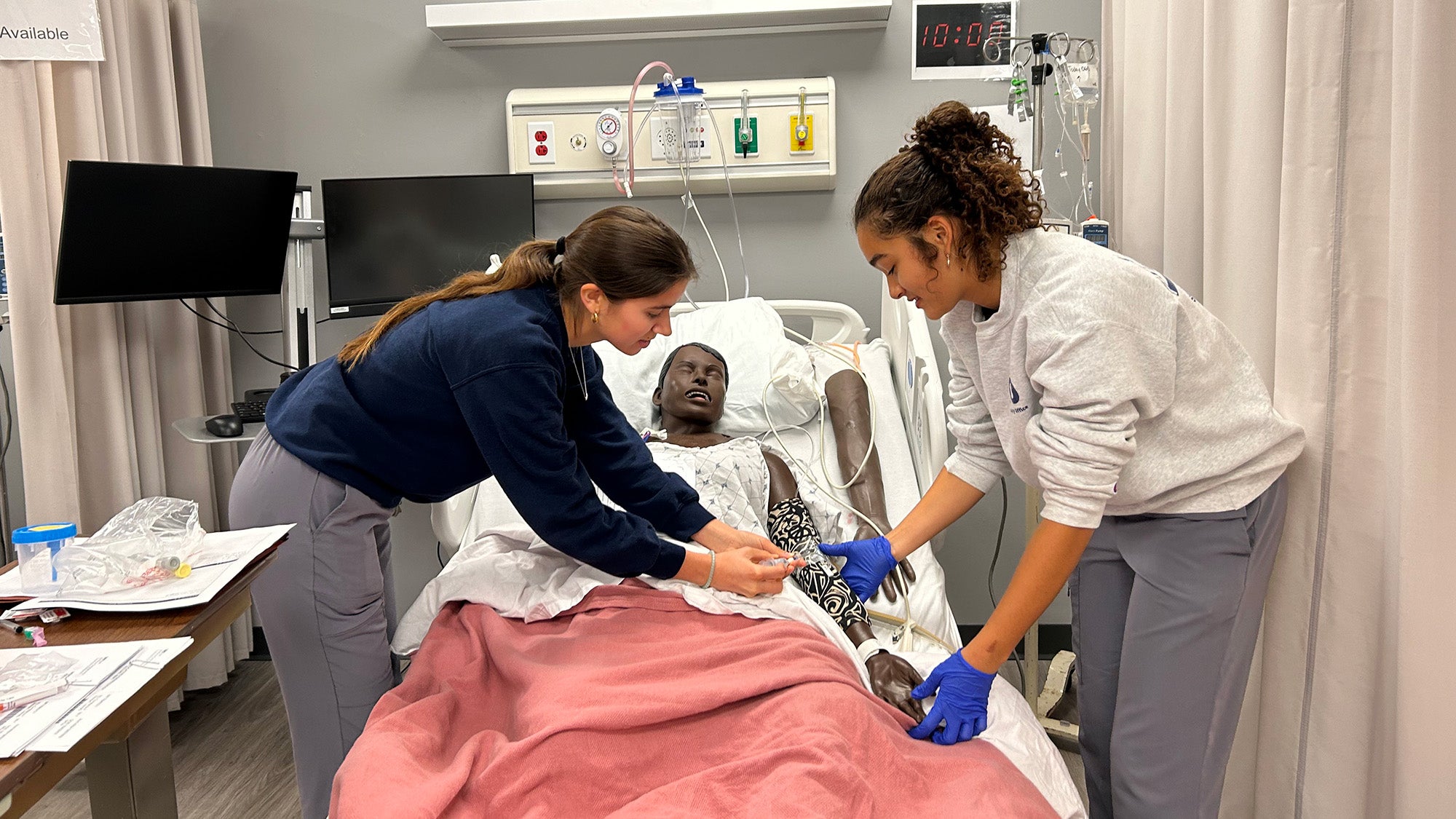 Two students take the blood pressure of one of the simulators in the Sim Lab