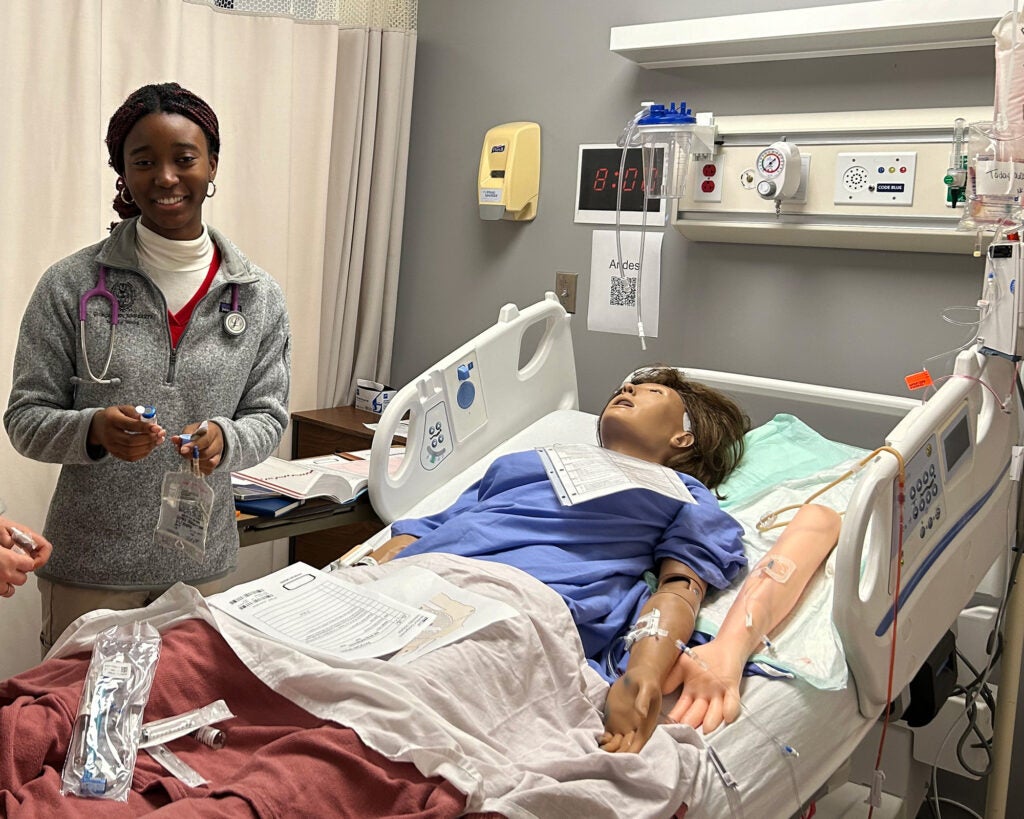 A Black student works on administering an IV to the simulation dummy in the Sim Lab