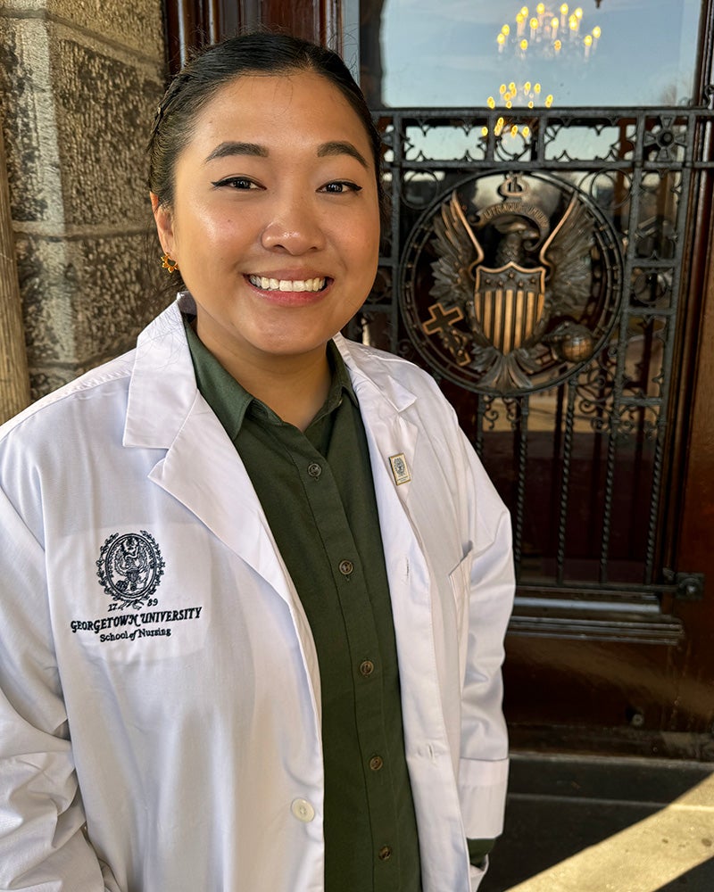 Jaclyn Sison in white coat outside Healy Hall's ornate doors