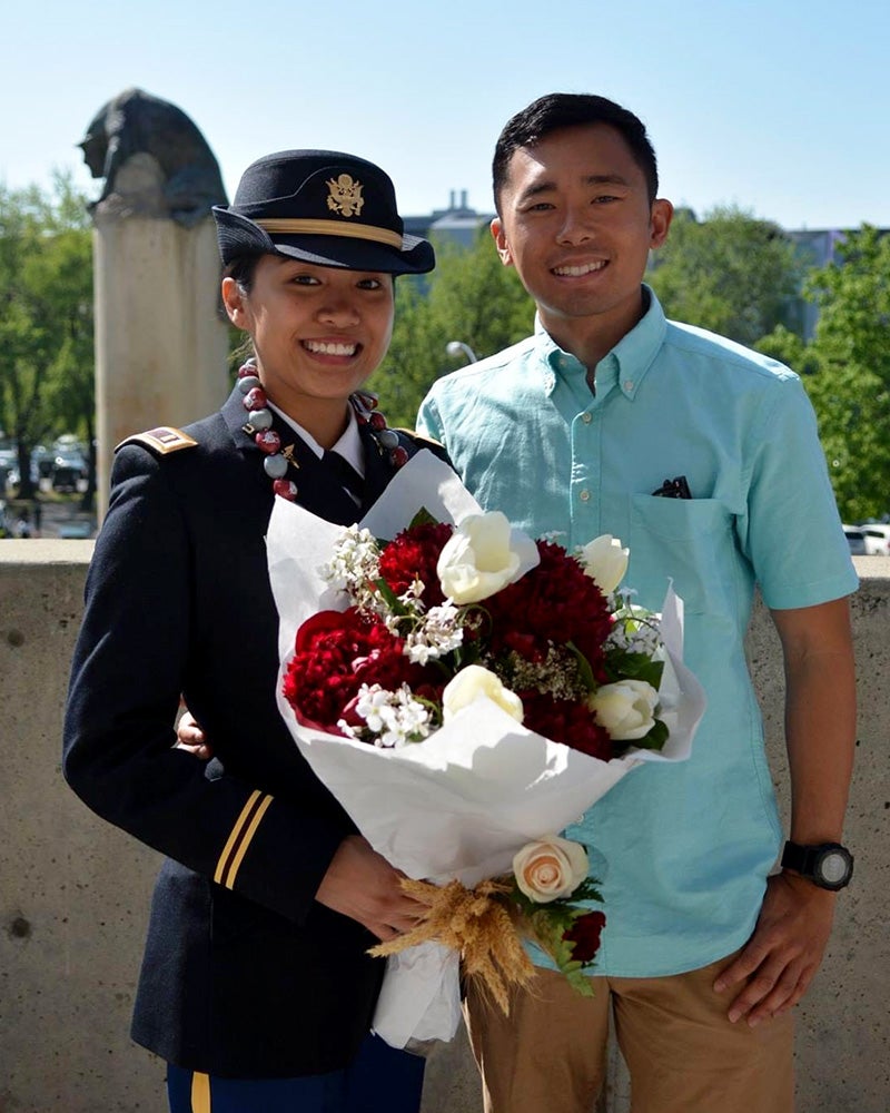 Jaclyn Sinson stands next to her husband, Sean, dressed in her Navy uniform and holding a large bouquet of flowers