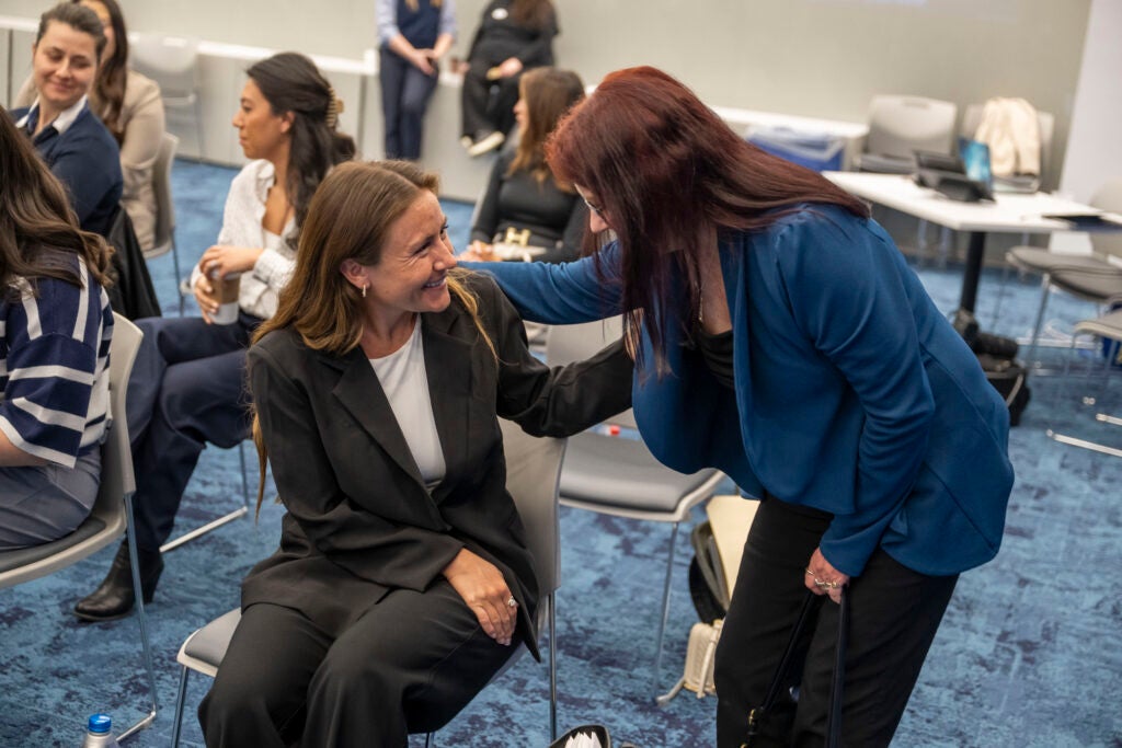 A faculty member standing and talking with a seated student.