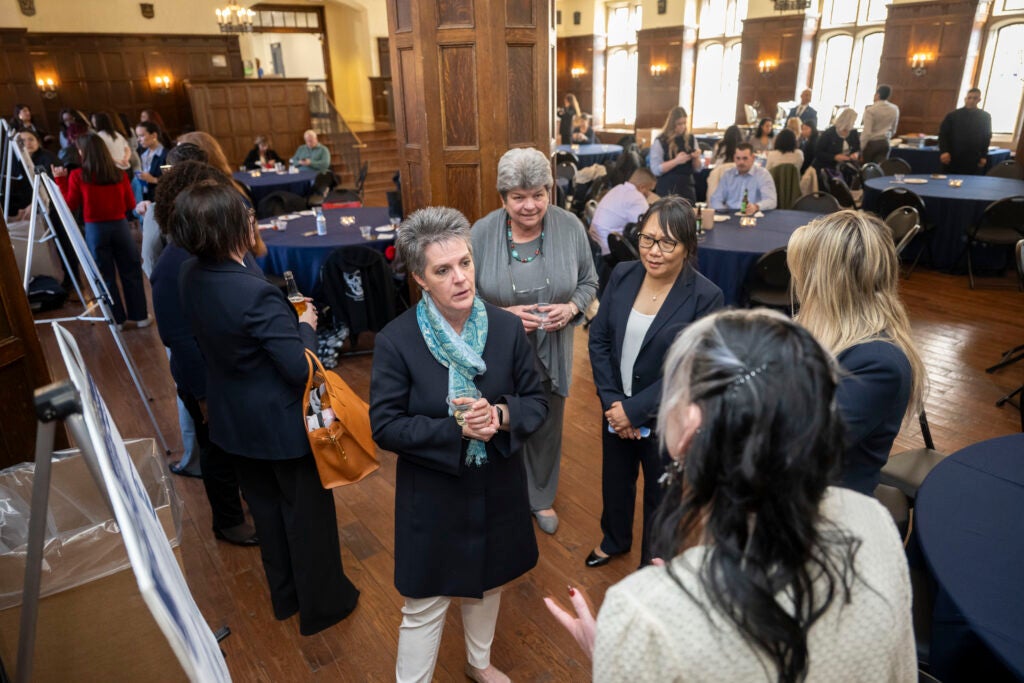 Faculty members stand and gather around a student's poster presentation.