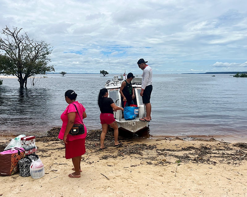 Four individuals load a boat with supplies along a sandy shoreline