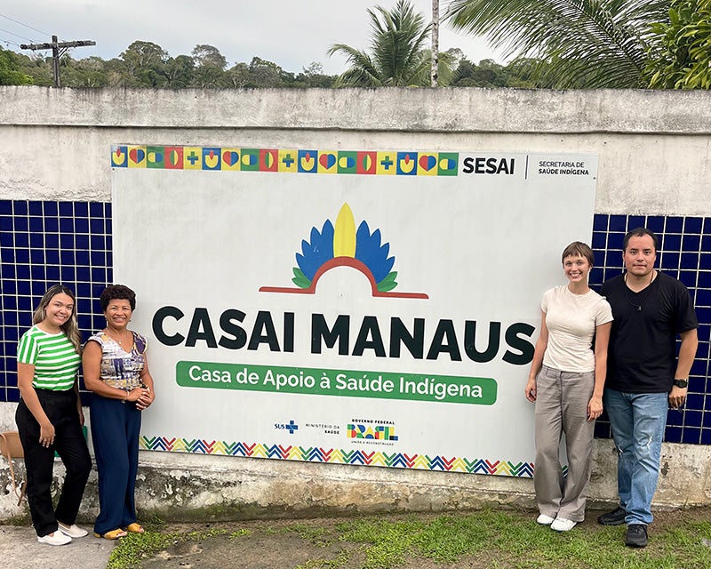 Meger stands with three other individuals in front of a mural on a wall for Casai Manaus with words in Portuguese
