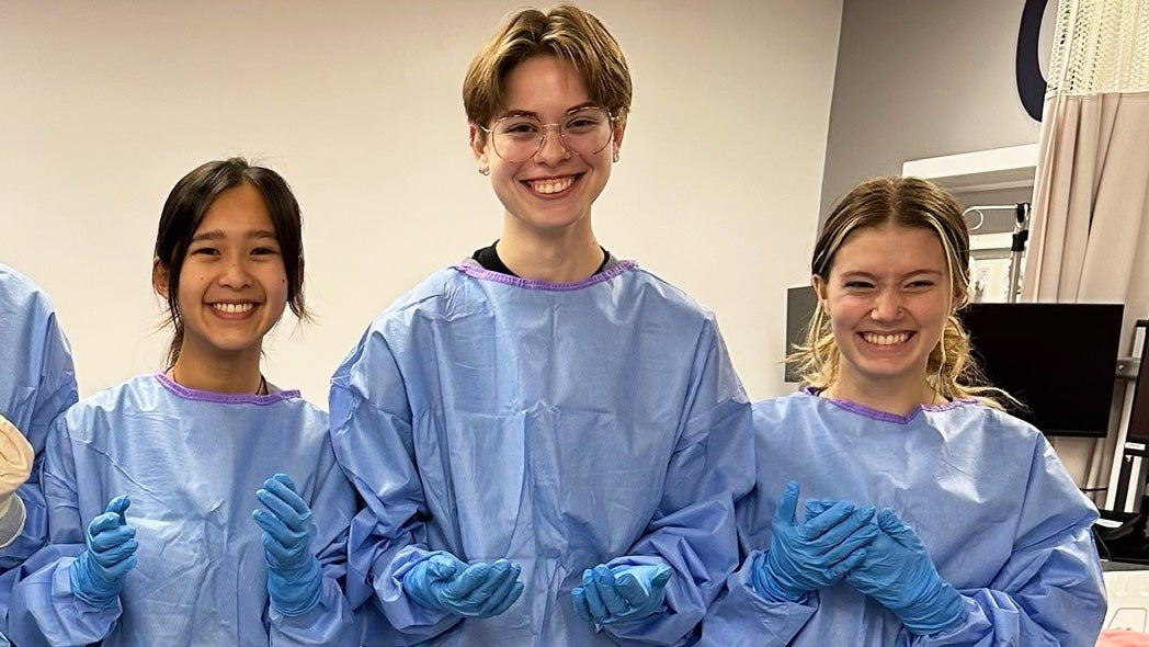 Three students garbed in personal protective gear stand together