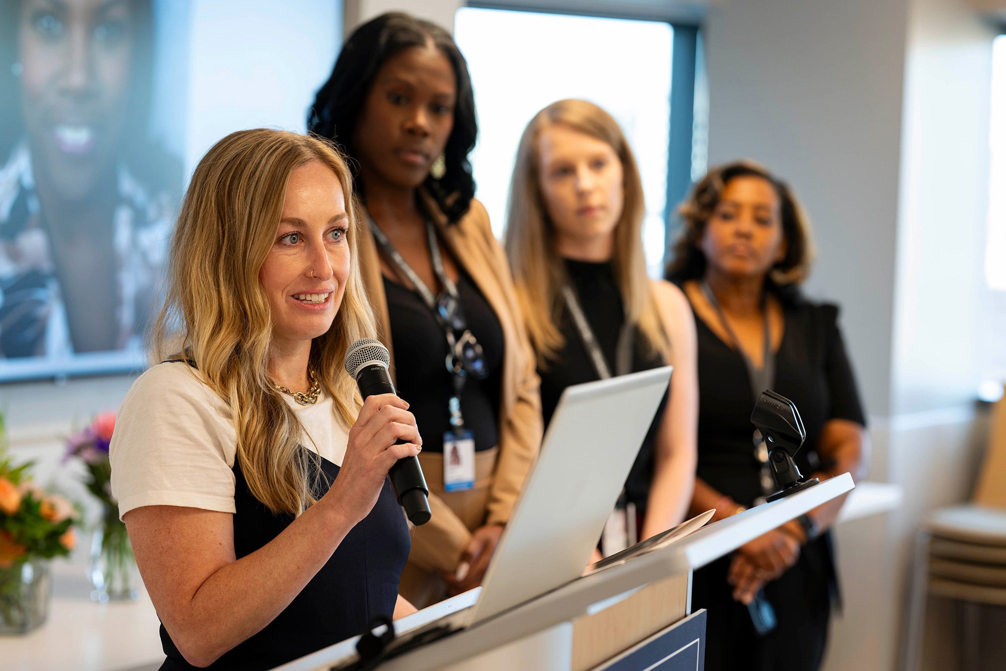 Kate Ellis speaks into a microphone while her three classmates stand in the background