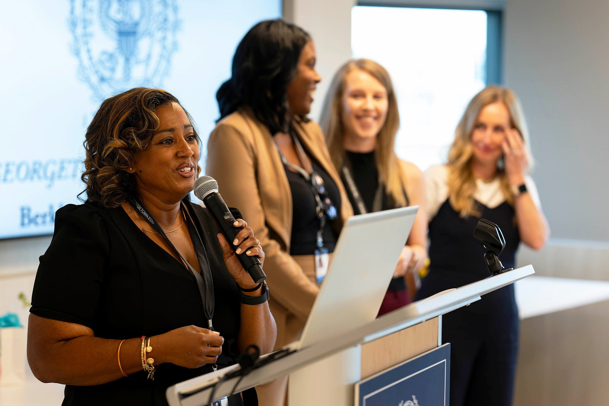 Kenyatta Hazlewood speaks into a microphone while her three classmates stand in the background