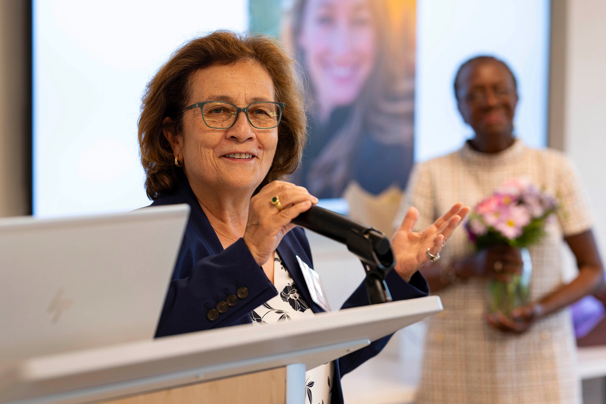 Maria Gomez speaks from a podium with Edilma Yearwood in the background