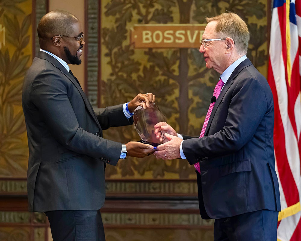 Christopher King presents Quint Studer with a glass award onstage in Gaston Hall