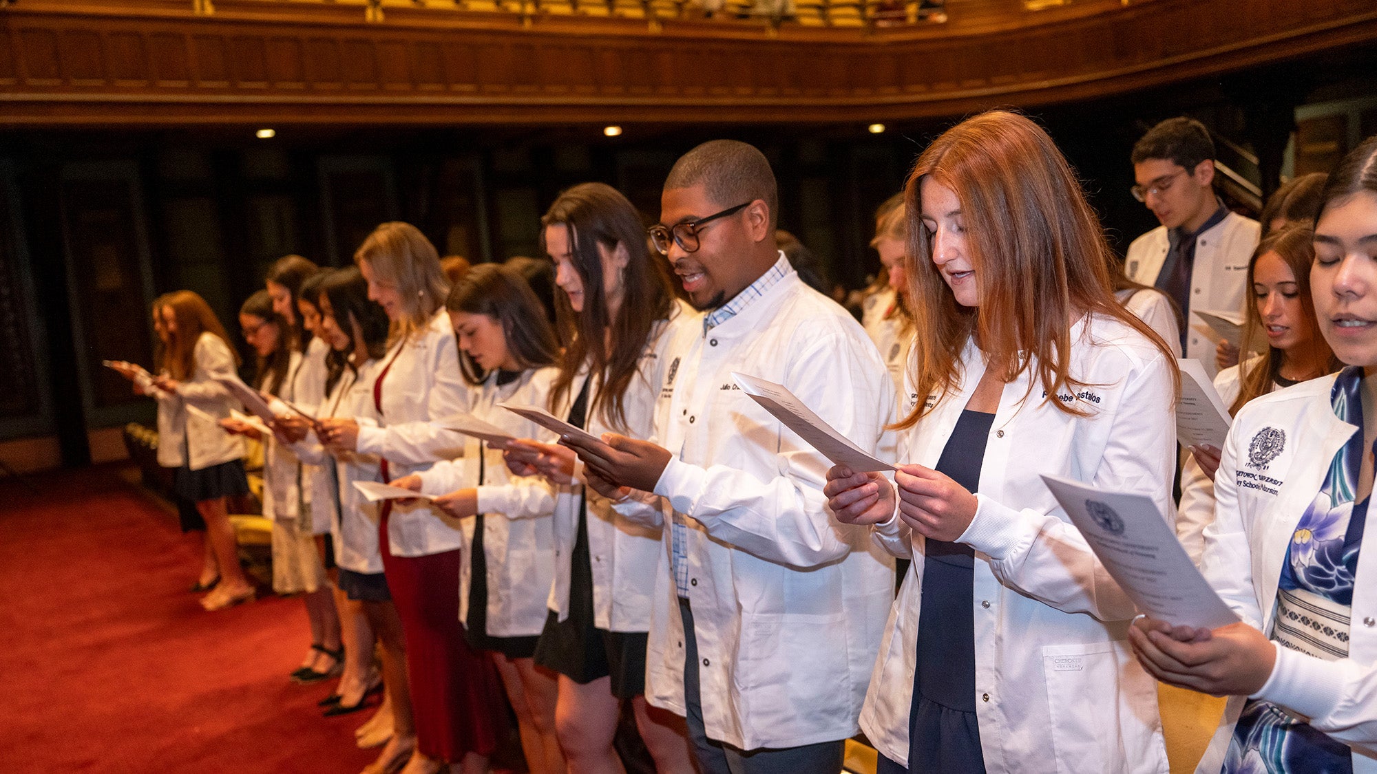 Nursing students stand in their new white coats and recite during the White Coat ceremony