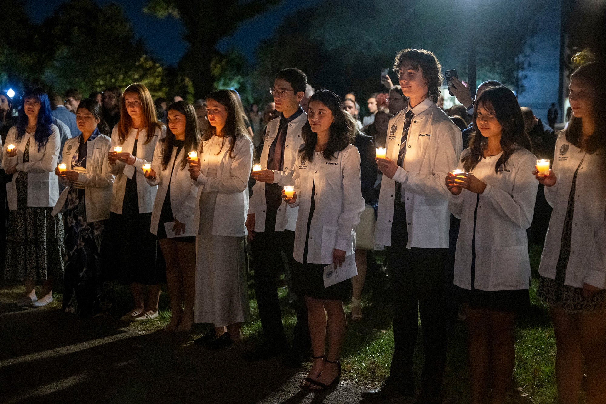 Students wearing white coats and holding lit candles stand in a line and participate in the ceremony