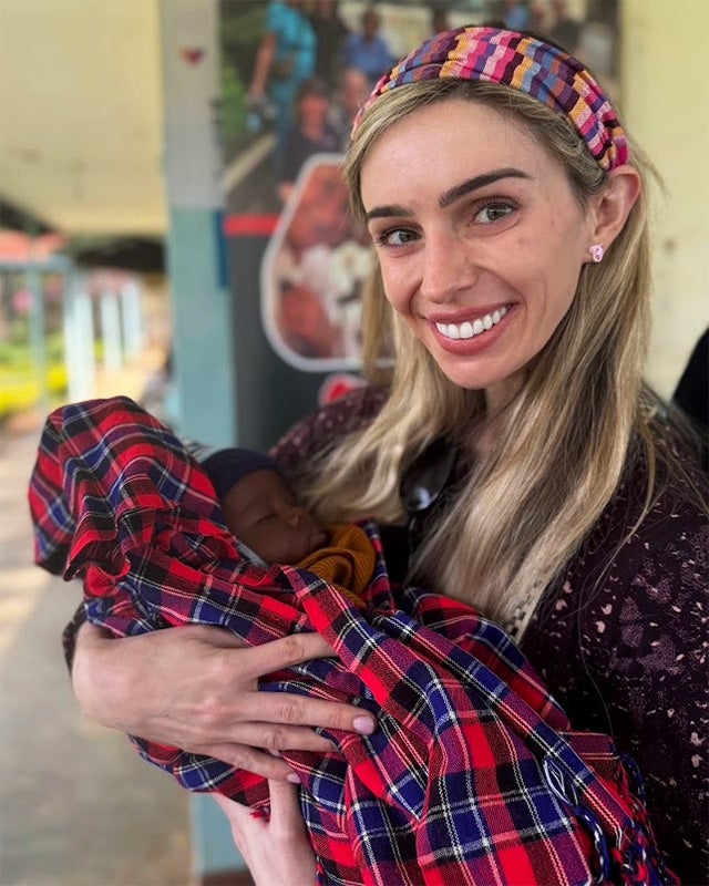 Alex holds a baby wrapped in a red plaid blanket