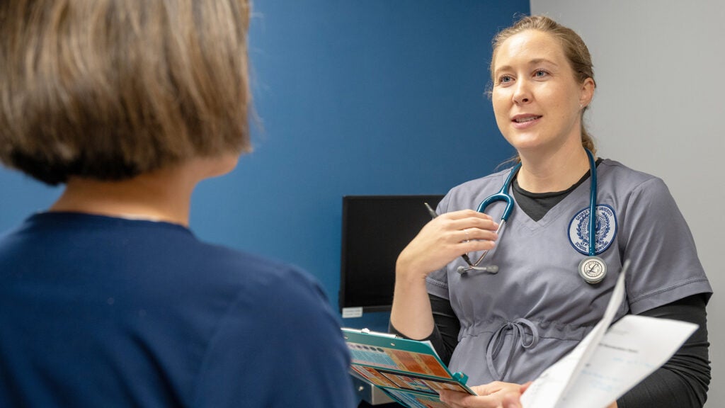An ABSN student in scrubs talks with an instructor in the SIM lab