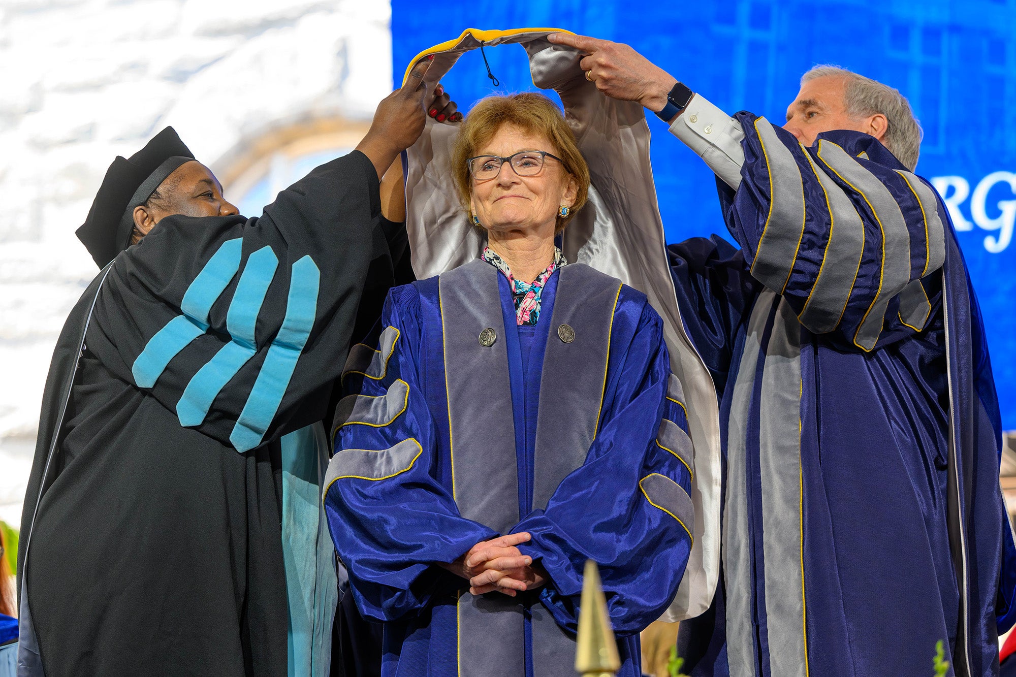 Dean Waite and Interim President Groves lift an honorary hood over Mary Wakefield's head and shoulders