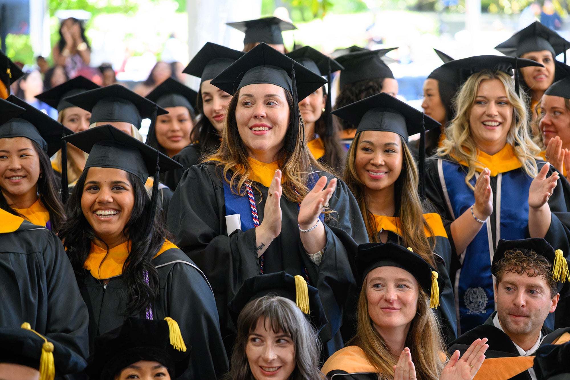 Students in caps and gowns stand together and applaud