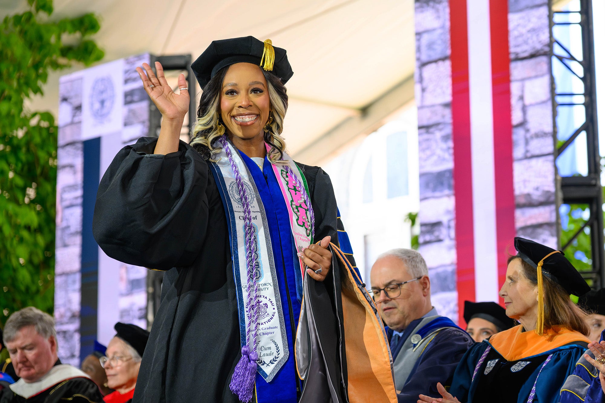 A graduate student walks across the stage and waves