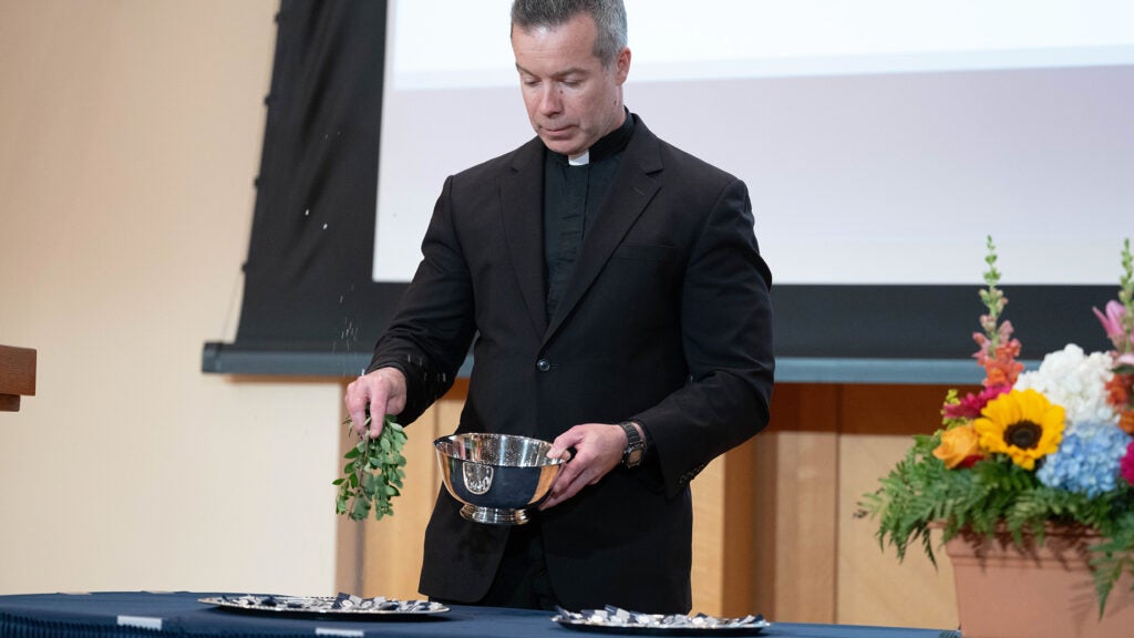 A priest shakes a sprig of herbs doused in holy water over platters of pins