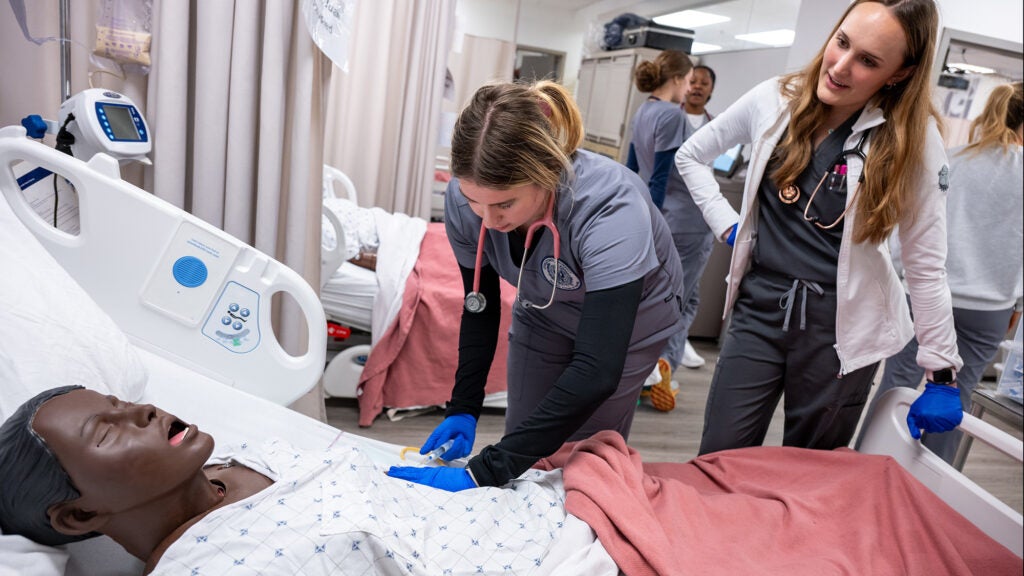 Two students interact with a SIM Lab mannequin