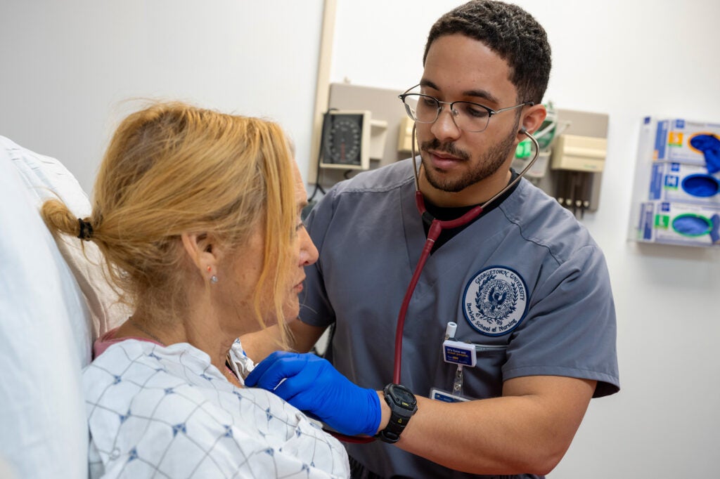 A male nursing student uses a stethoscope to listen to the heartbeat of a standardized patient