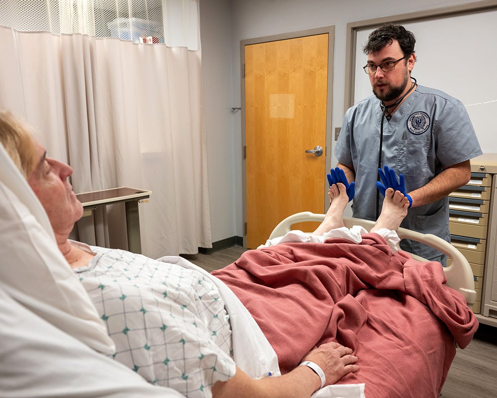 Matthew Small presses his palms against the feet of a patient lying in a bed