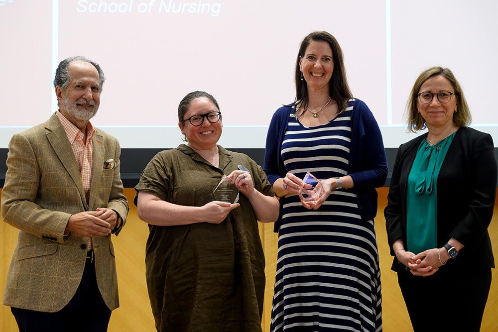 Four individuals stand together, two holding crystal awards