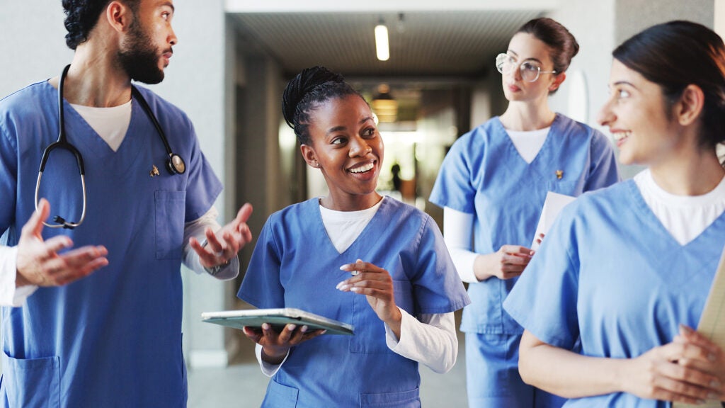 A group of four students wearing medical scrubs talk while walking through a hallway