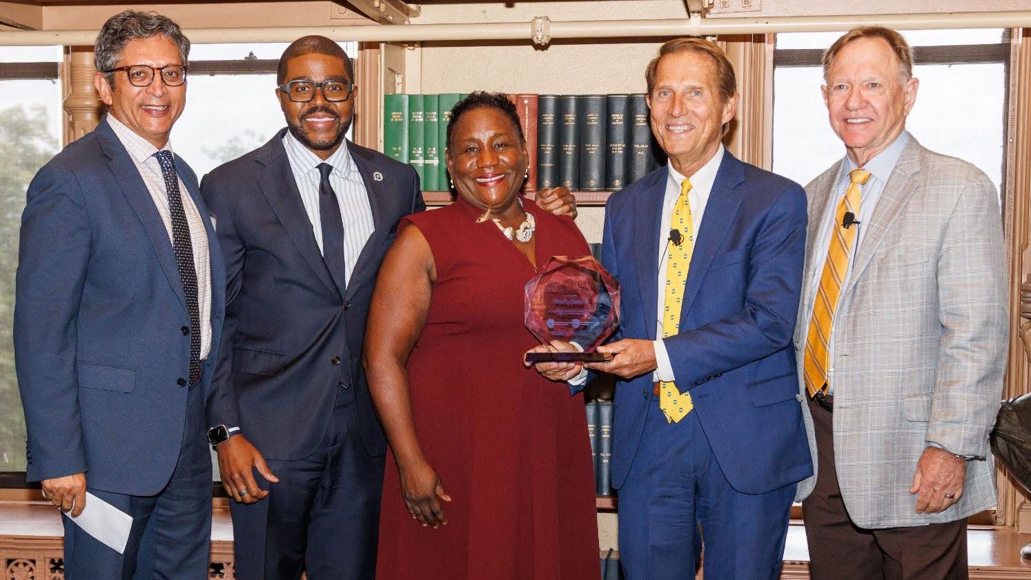 Group of five people stand smiling as an award is given.